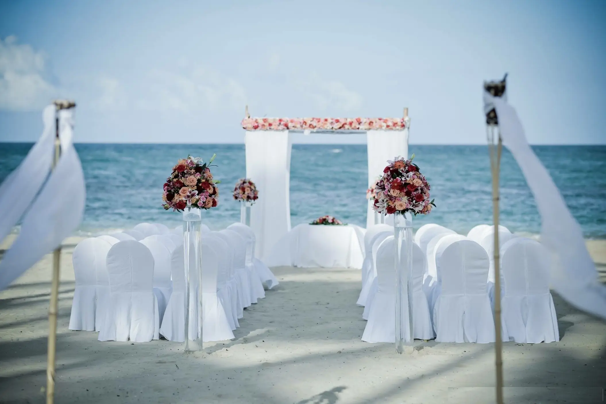 Beachfront wedding ceremony with white chairs and pink floral arch at Breathless Punta Cana, Punta Cana