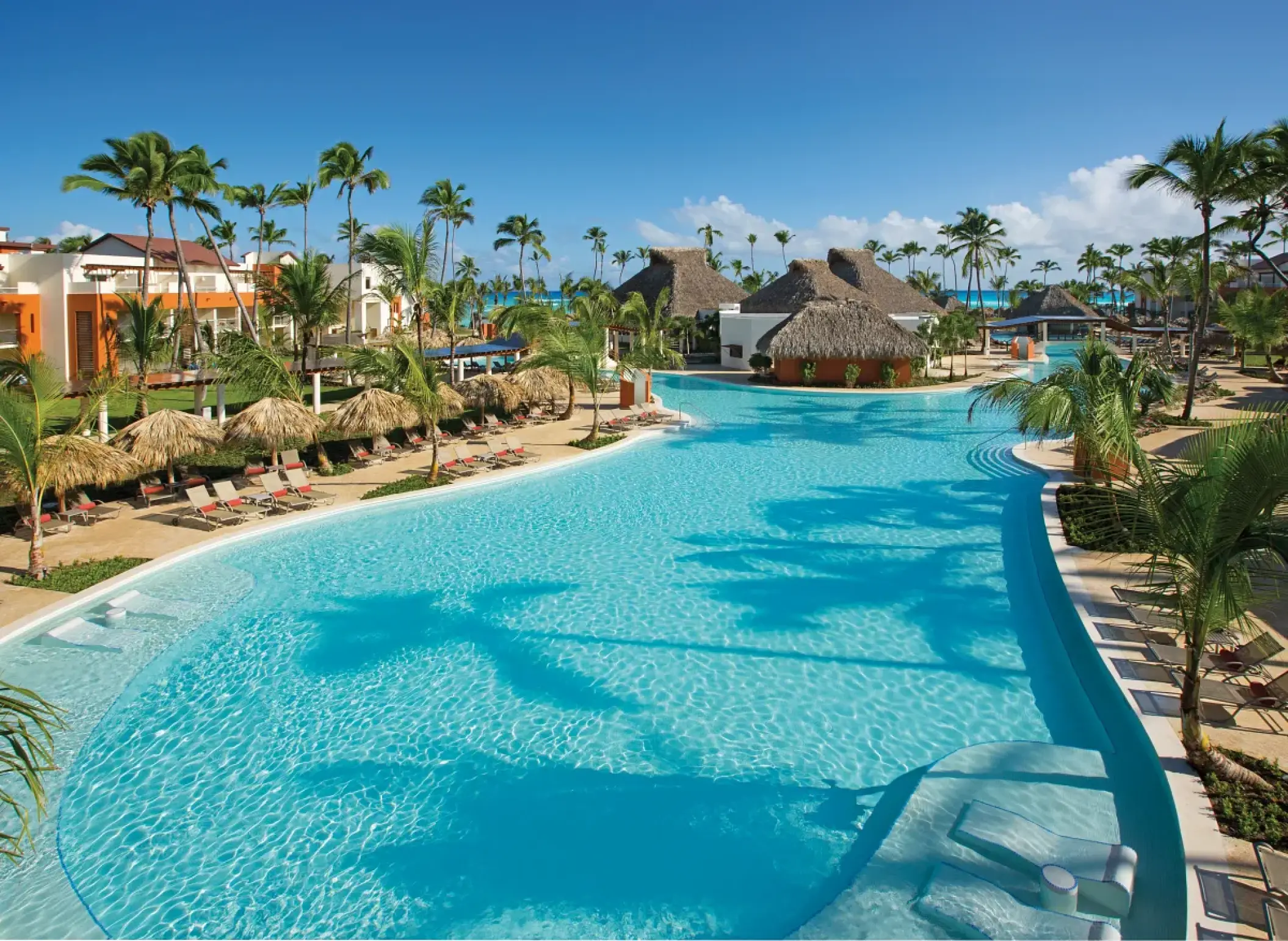 Breathless Punta Cana main pool surrounded by palm trees and thatched palapas, Punta Cana