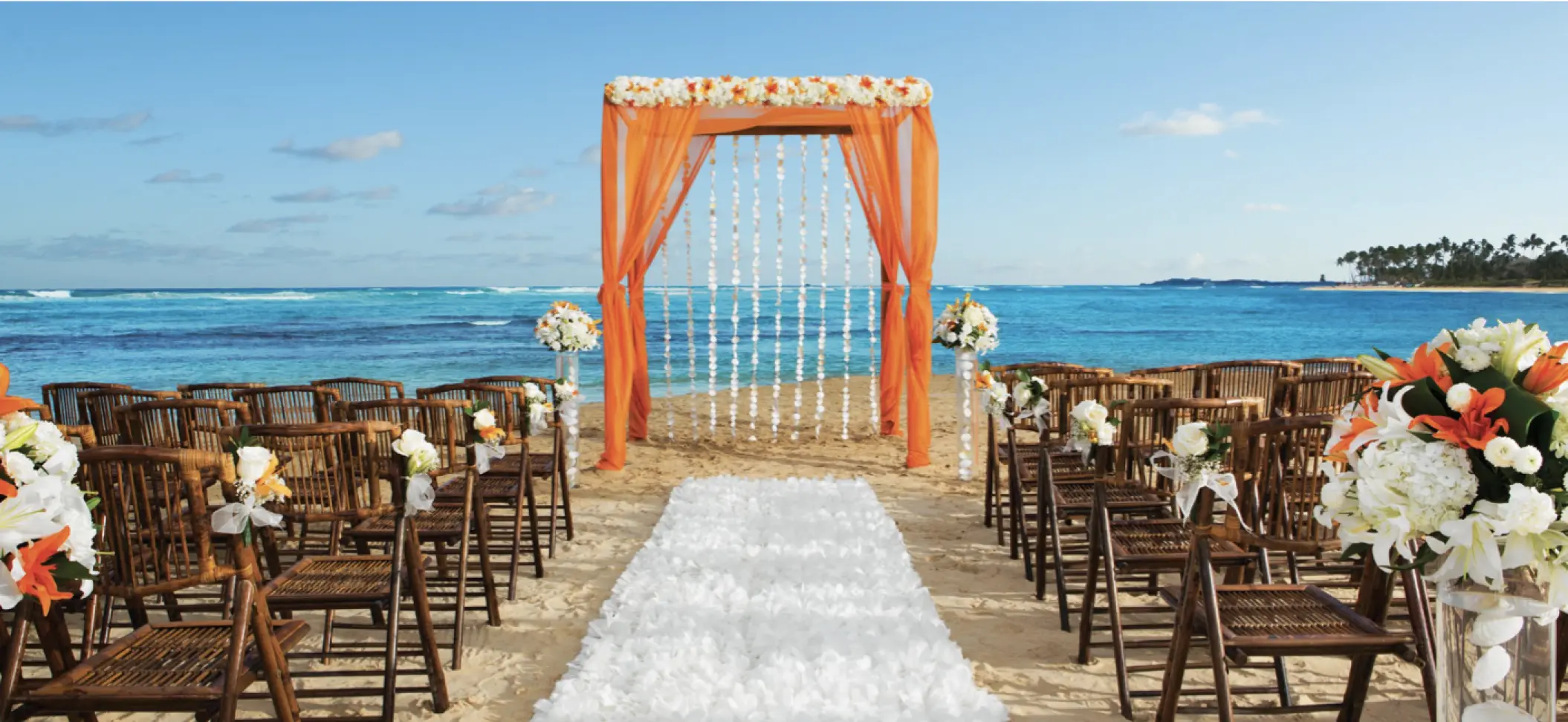 Beachfront wedding ceremony with orange drapes and white aisle runner at Breathless Riviera Cancun, Riviera Maya