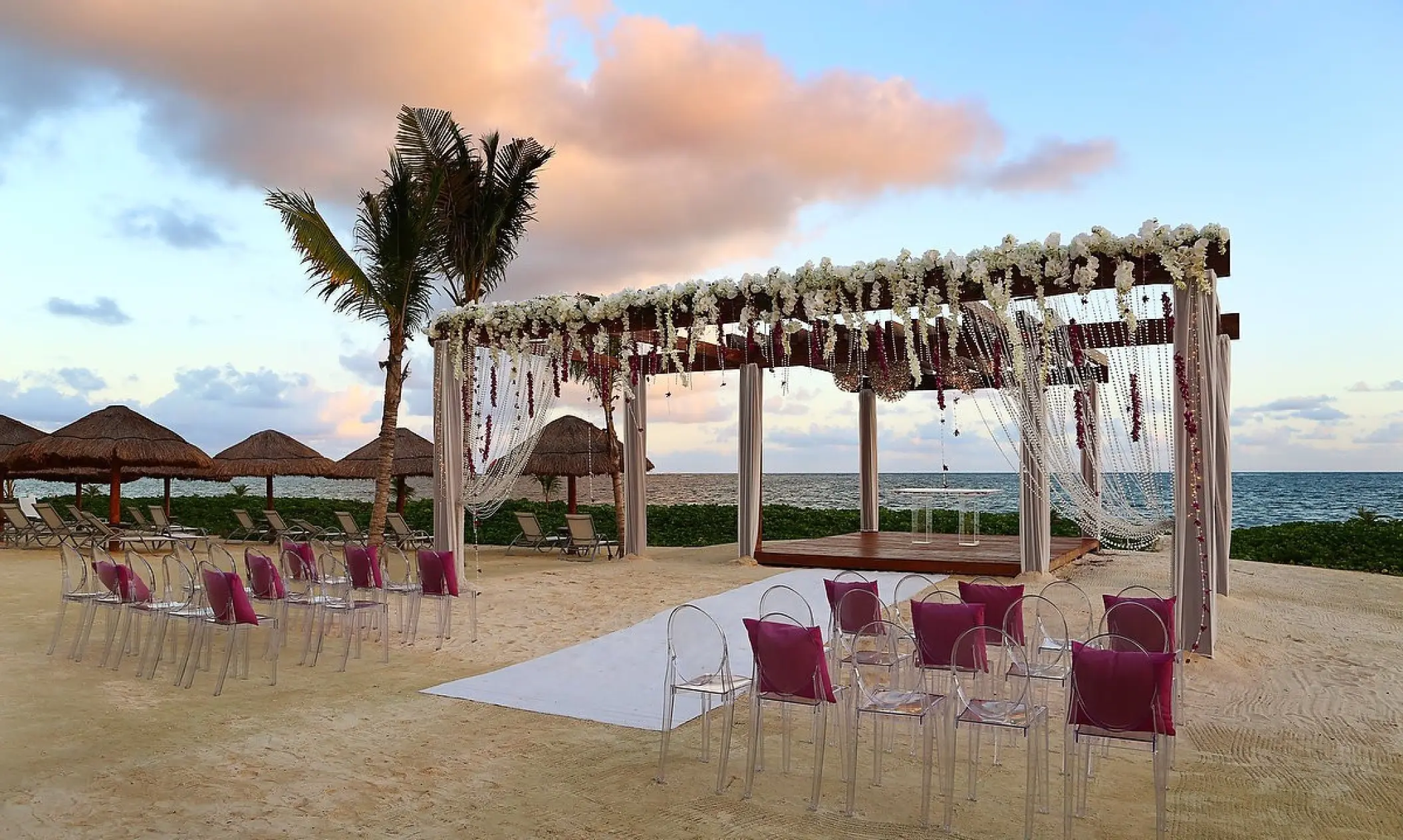 Beach wedding ceremony setup with white floral pergola and clear chairs at Breathless Riviera Cancun, Riviera Maya
