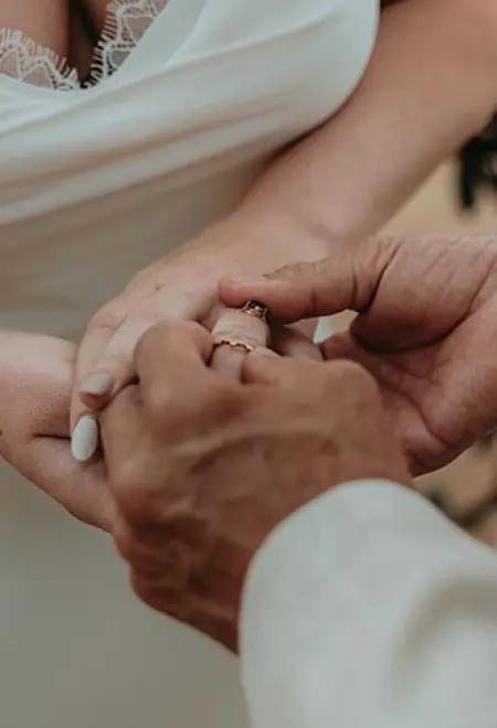 Close-up of David placing a gold wedding band on Carrie's finger during their ceremony