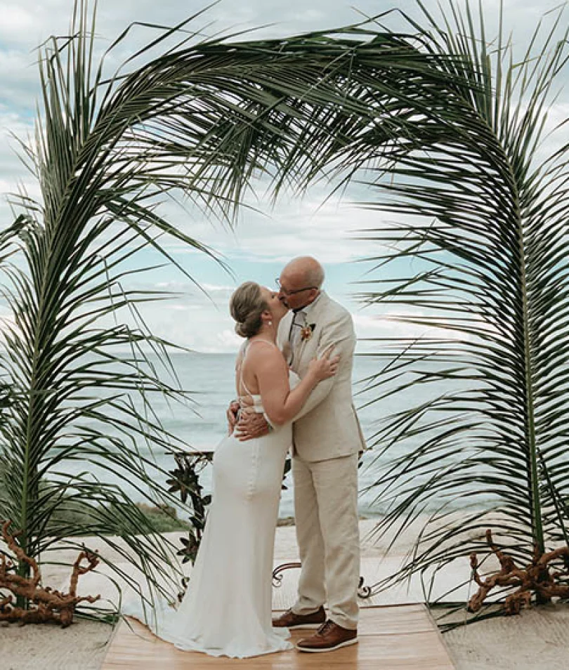 Gorm and bride's first kiss underneath a beatiful palmtree made arch
