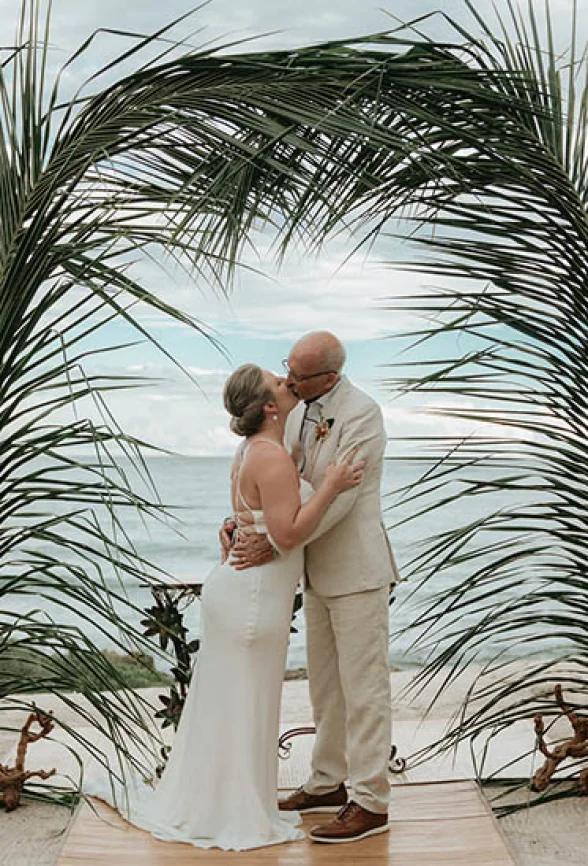Gorm and bride's first kiss underneath a beatiful palmtree made arch