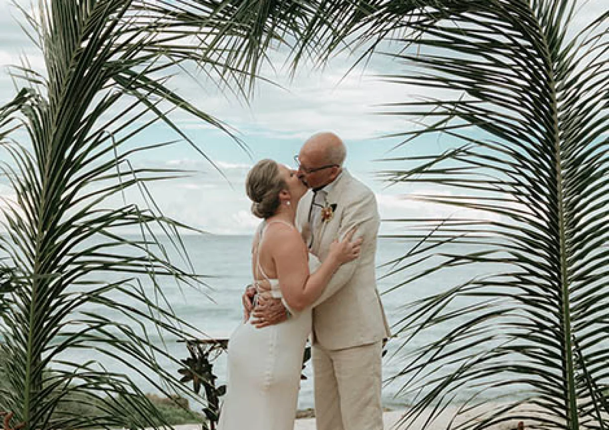 Gorm and bride's first kiss underneath a beatiful palmtree made arch