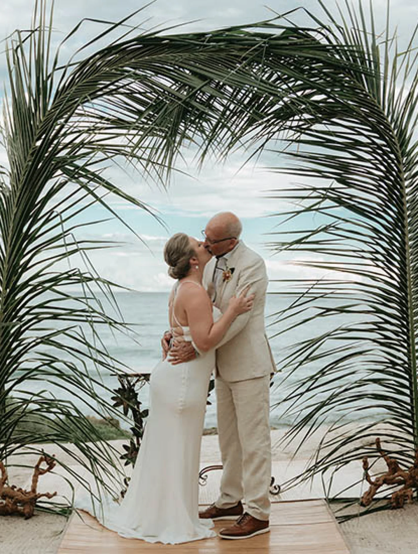 Gorm and bride's first kiss underneath a beatiful palmtree made arch
