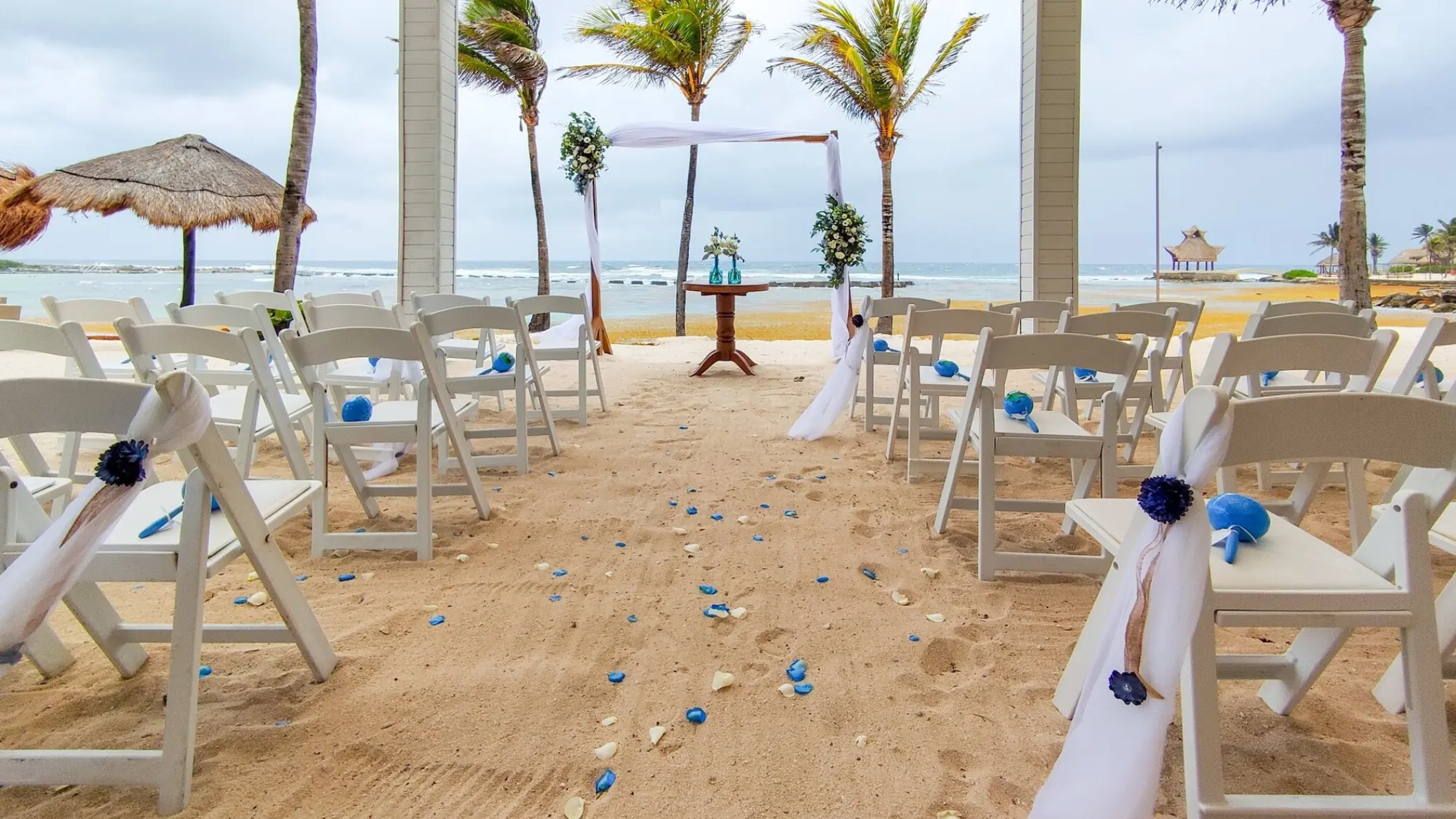 Beachfront wedding ceremony with white chairs and floral arch at Catalonia Grand Costa Mujeres, Cancun