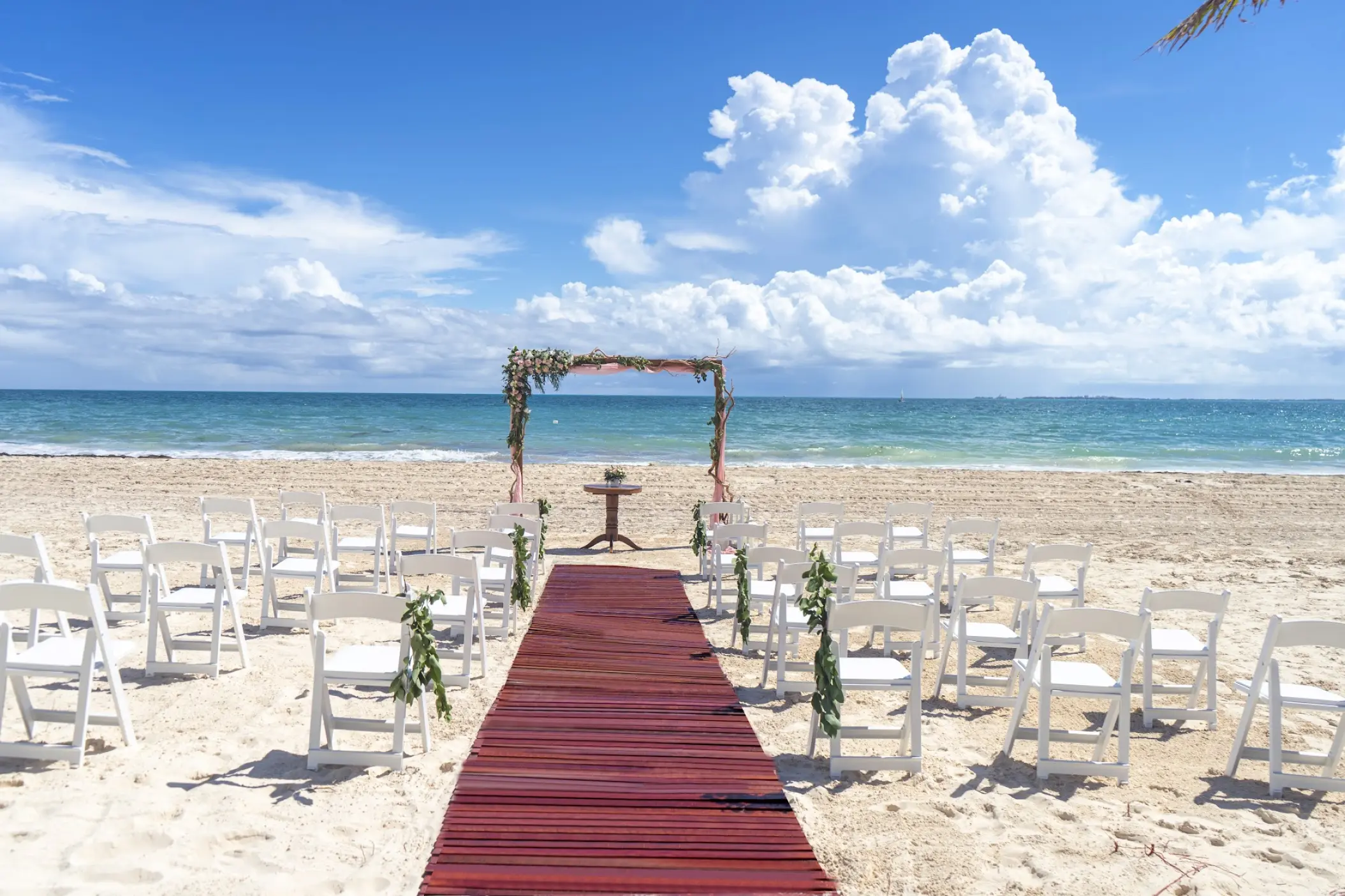 Beachfront wedding ceremony with a red aisle runner and floral arch at Catalonia Grand Costa Mujeres, Cancun