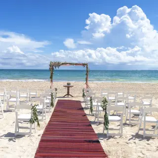 Beachfront wedding ceremony with a red aisle runner and floral arch at Catalonia Grand Costa Mujeres, Cancun