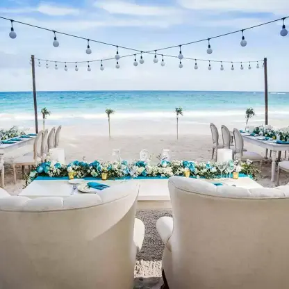 Beachfront wedding reception setup with string lights and white floral runners at Catalonia Royal Tulum