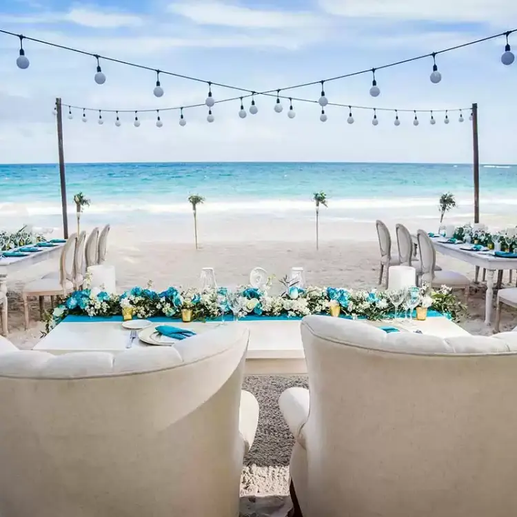 Beachfront wedding reception setup with string lights and white floral runners at Catalonia Royal Tulum