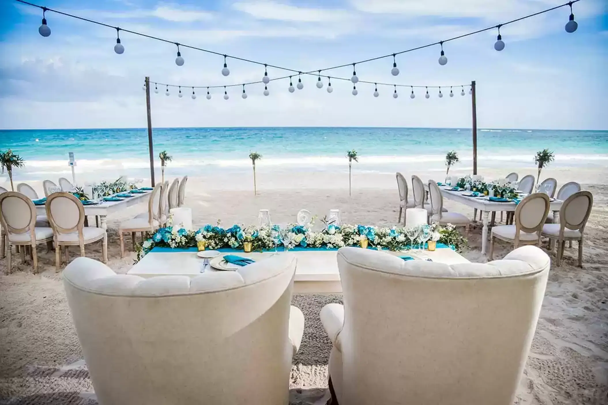 Beachfront wedding reception setup with string lights and white floral runners at Catalonia Royal Tulum