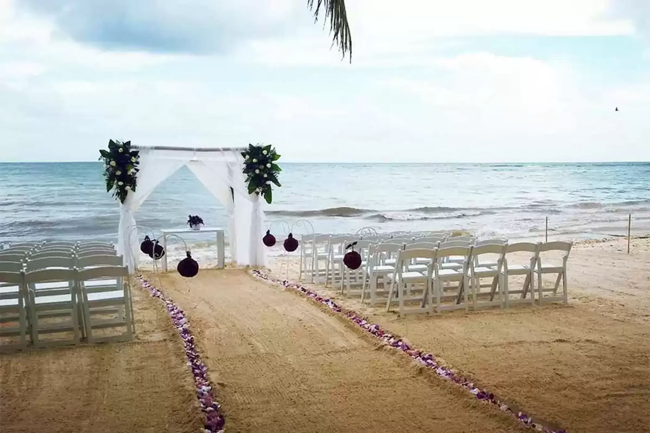 Beachfront wedding ceremony setup with white arch and petal aisle at Catalonia Royal Tulum