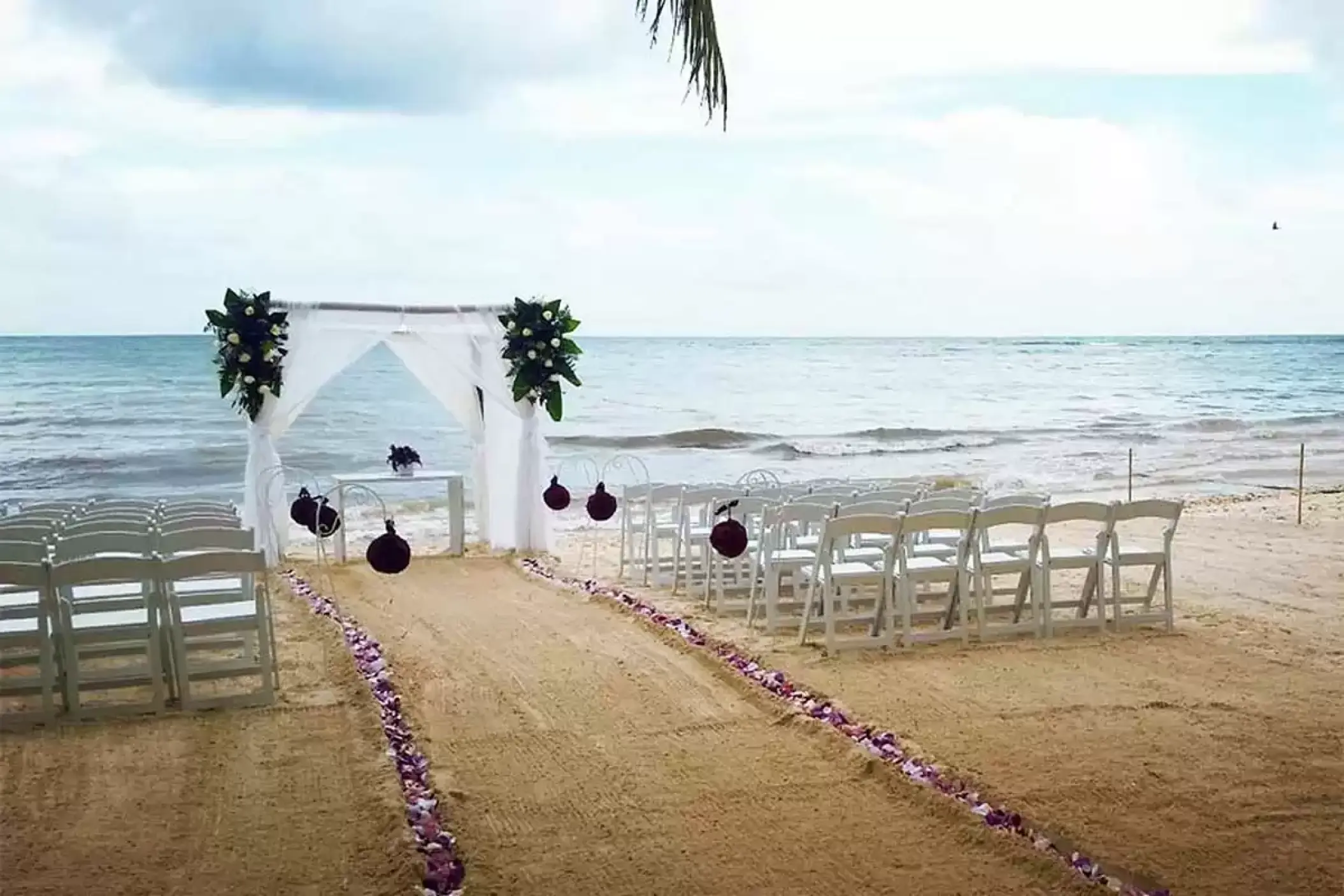 Beachfront wedding ceremony setup with white arch and petal aisle at Catalonia Royal Tulum