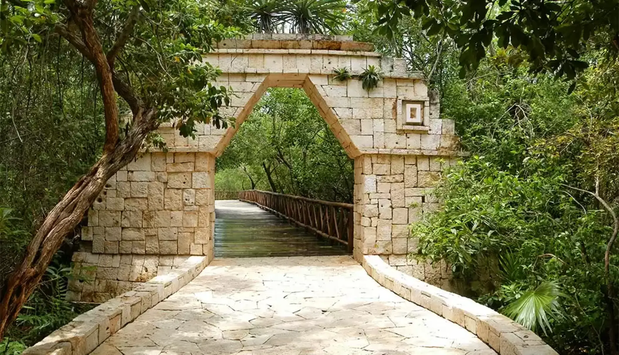 Stone archway leading to a wooden bridge through tropical jungle at Catalonia Royal Tulum