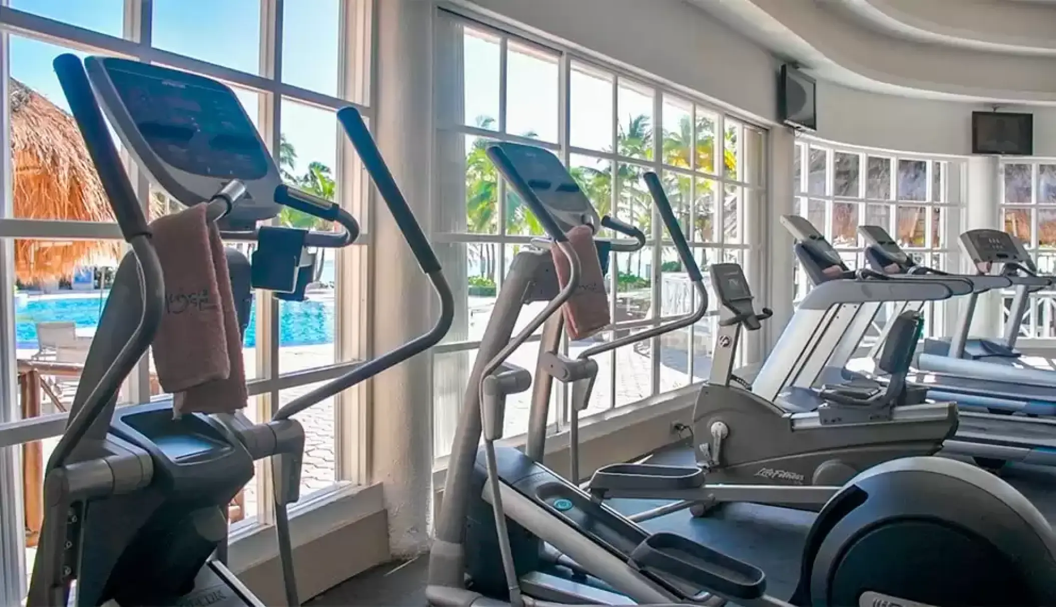 Catalonia Royal Tulum gym with cardio machines facing large windows and a pool view, Tulum