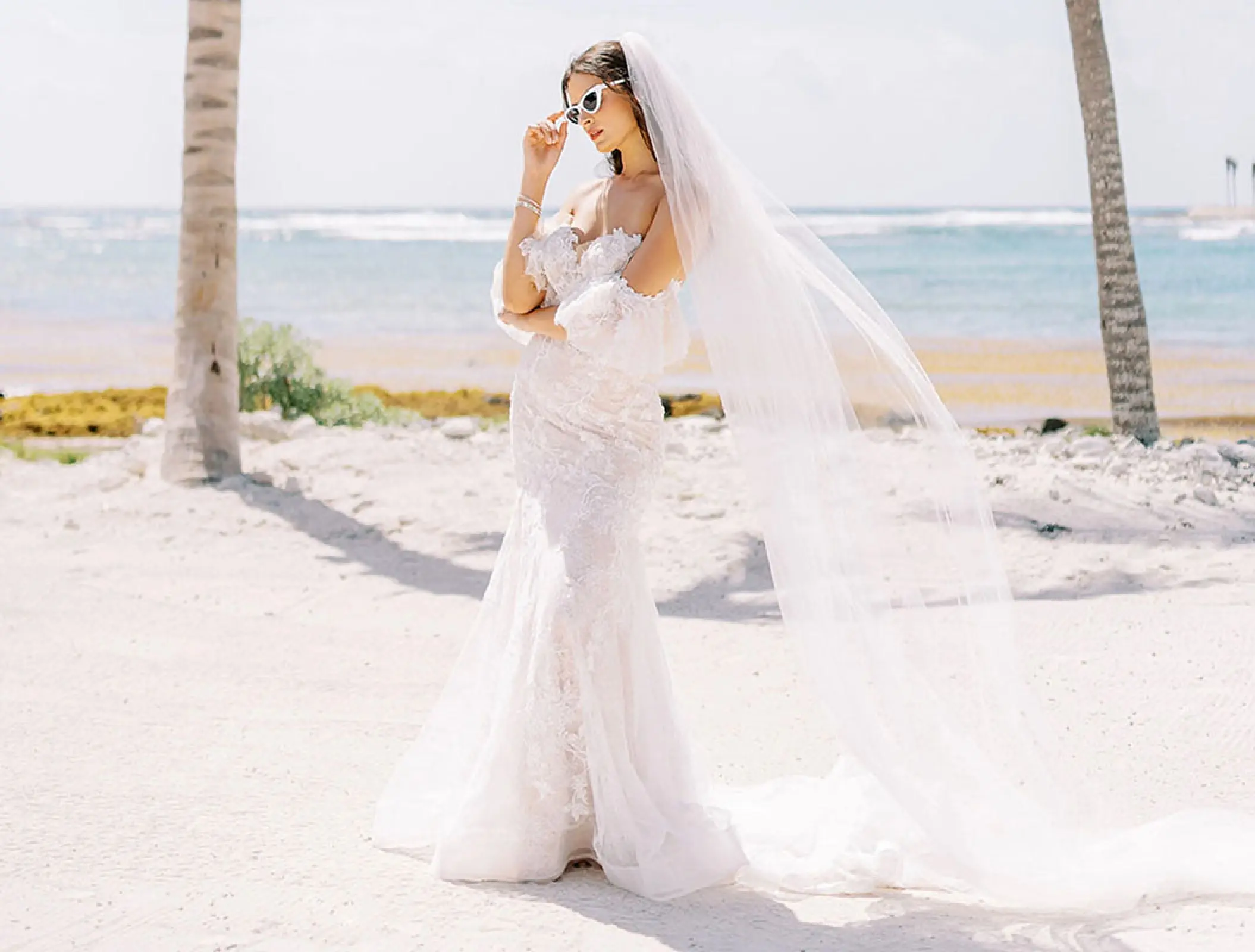 Bride in a white lace dress and sunglasses posing on the beach at Conrad Tulum, Tulum