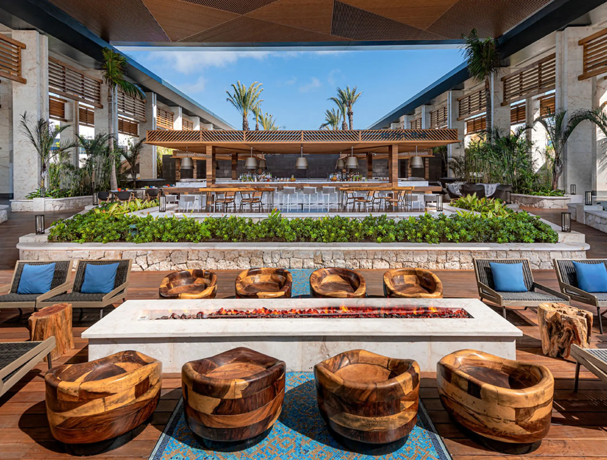 Outdoor lounge area with fire pit and wooden seating at Conrad Tulum, Tulum