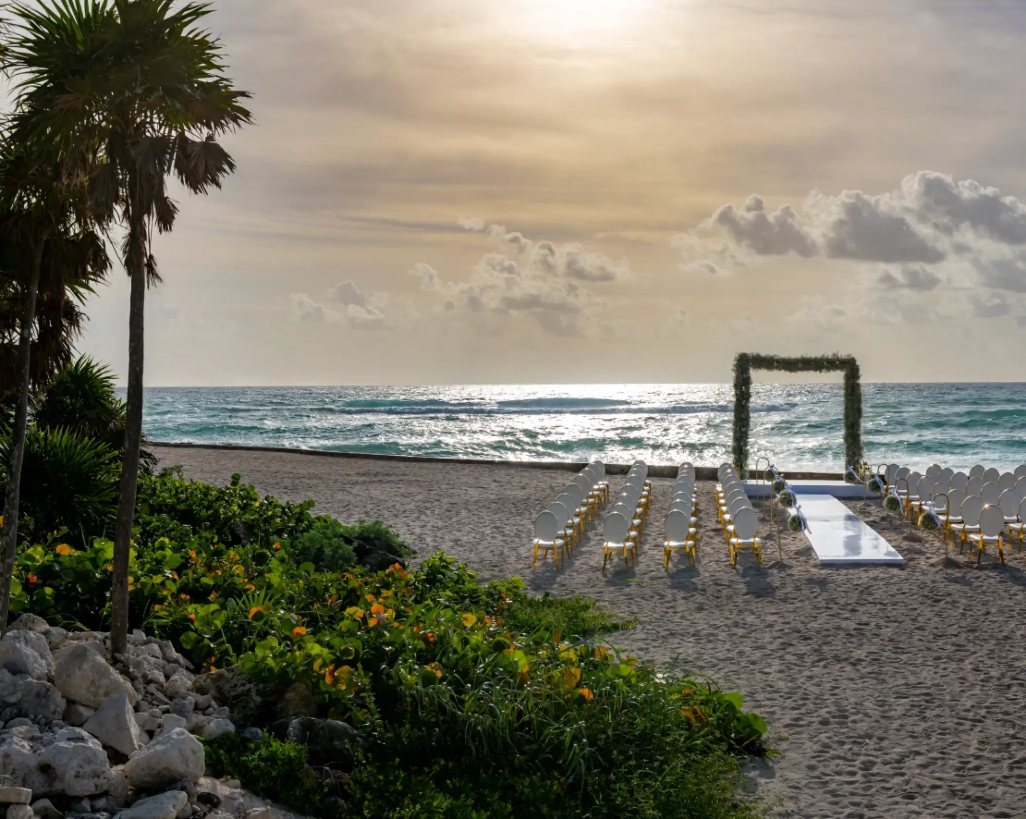 Beachfront wedding ceremony setup with white chairs and floral arch at Conrad Tulum, Tulum