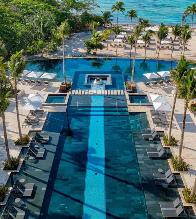 Aerial view of the long outdoor swimming pool and beachfront palm trees at Conrad Tulum, Tulum