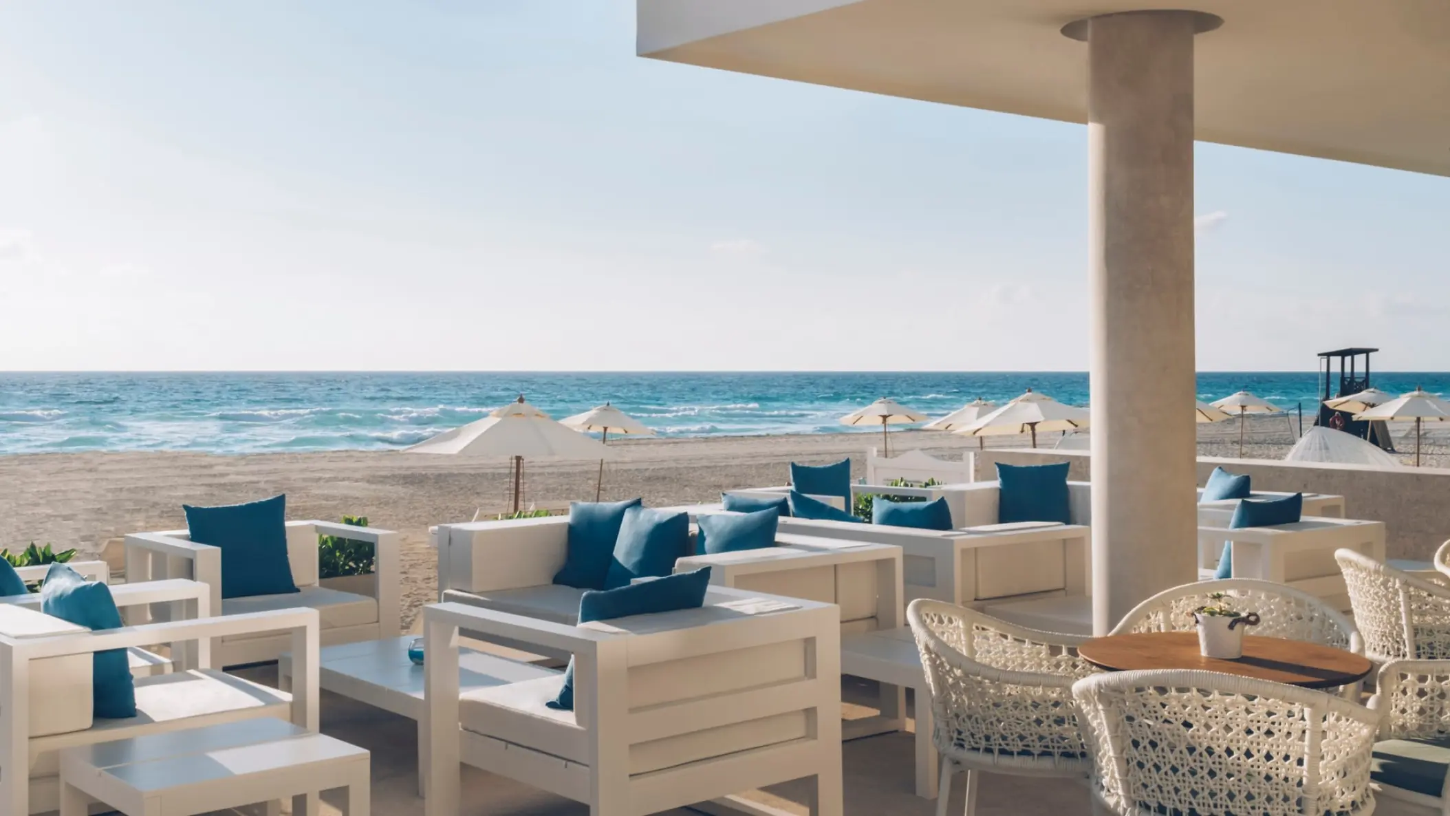 Beachfront restaurant seating area with white furniture and blue cushions at Coral Level Iberostar Cancun