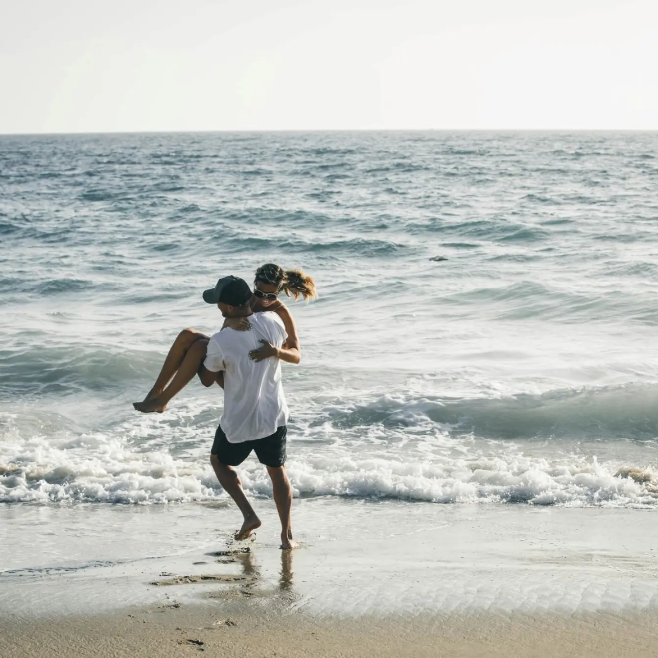 Man carrying a woman through the surf on a beach in Negril