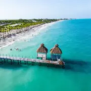 Aerial view of a wooden pier with palapa huts extending into turquoise water in Mexico