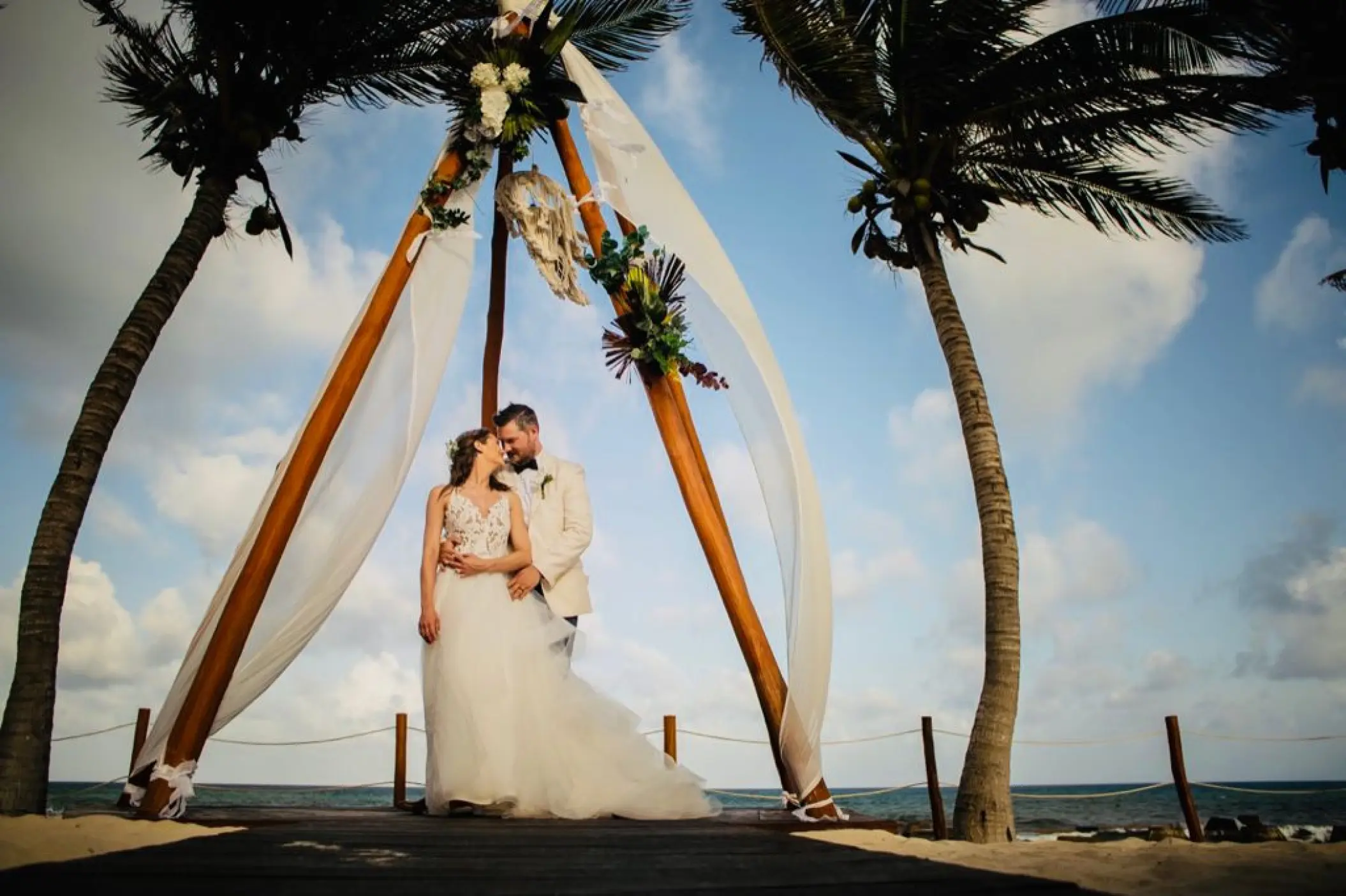 The couple posing under a wooden tepee ceremony arch at El Dorado Royale, Riviera Maya
