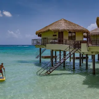 Overwater bungalows at El Dorado Maroma above turquoise water with a paddleboarder, Riviera Maya