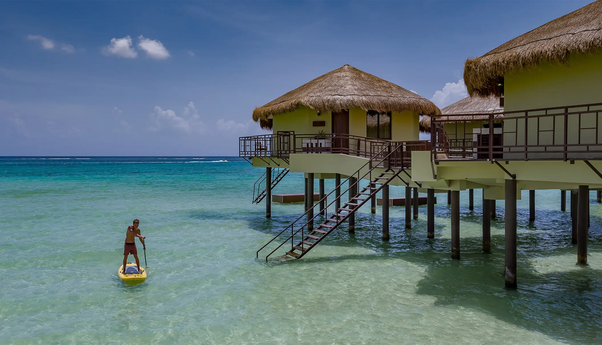 Overwater bungalows at El Dorado Maroma above turquoise water with a paddleboarder, Riviera Maya
