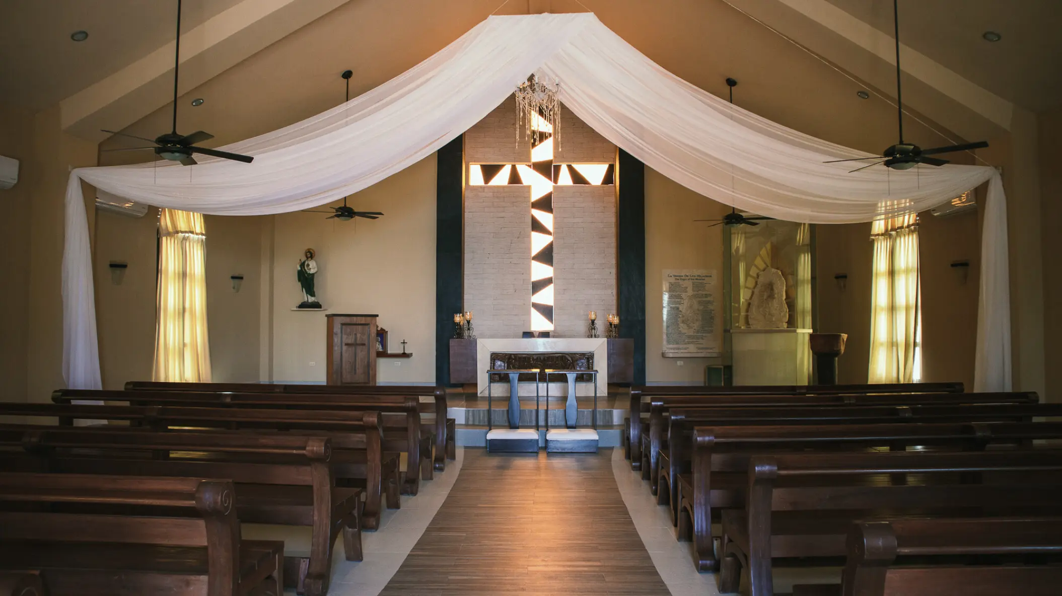 Chapel wedding ceremony setup with wooden pews and white fabric draping at El Dorado Royale, Riviera Maya