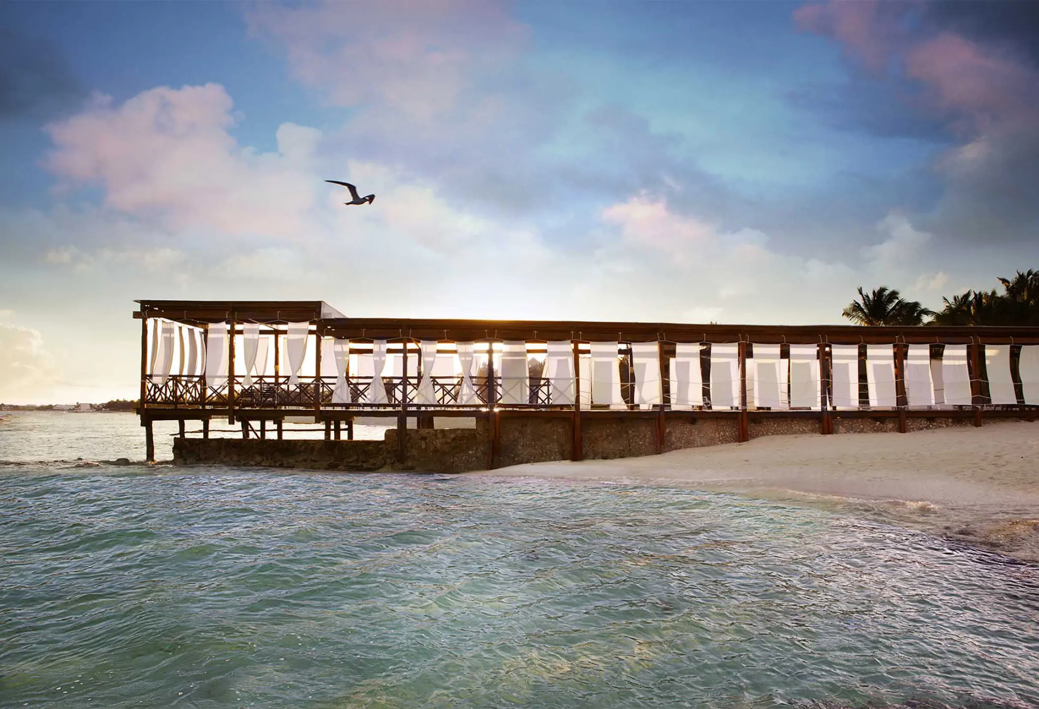 Wooden beachfront dining deck with white curtains at El Dorado Royale, Riviera Maya