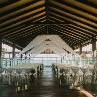 Covered deck wedding ceremony with white draping and lanterns at El Dorado Royale, Riviera Maya