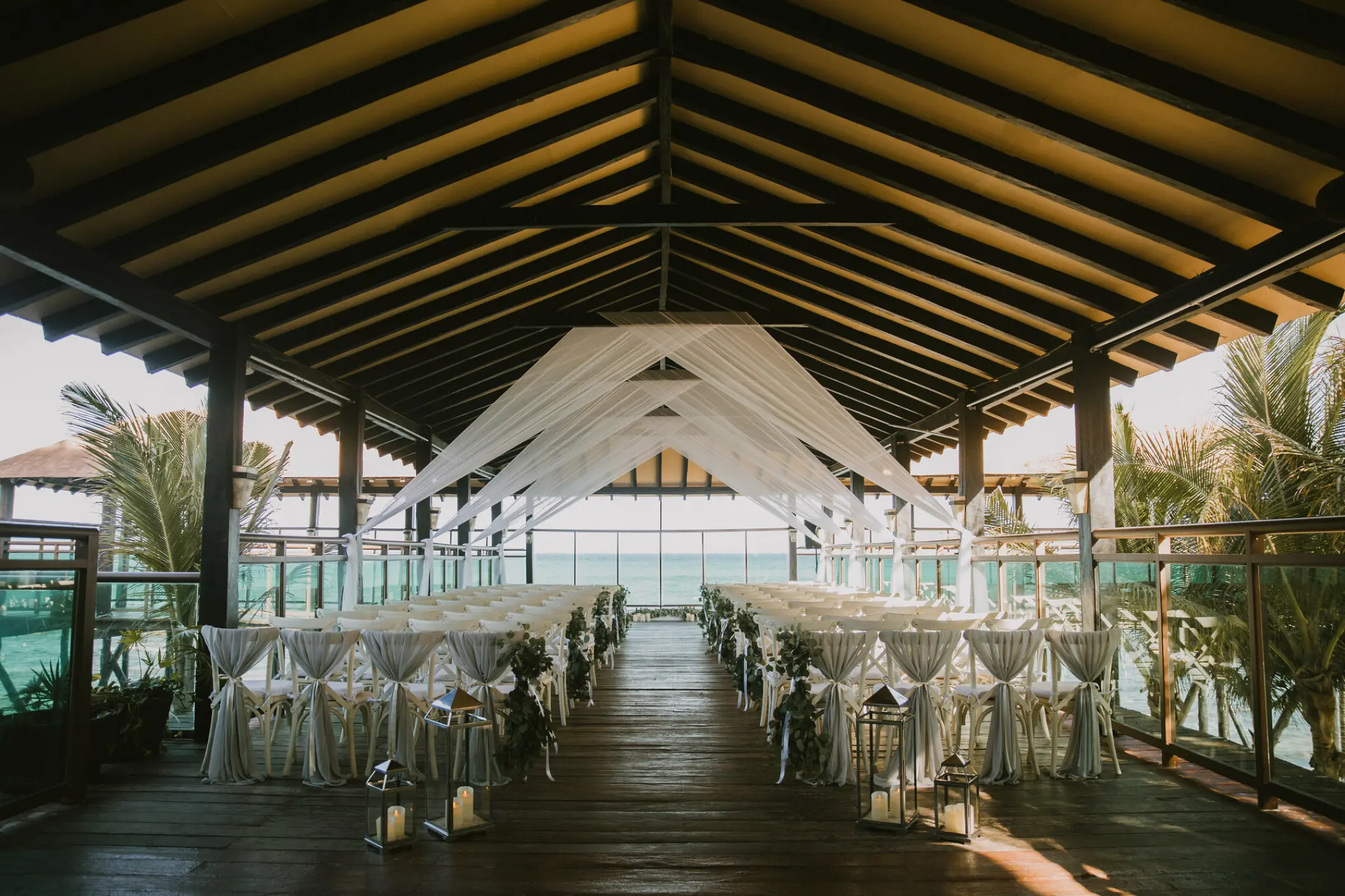 Covered deck wedding ceremony with white draping and lanterns at El Dorado Royale, Riviera Maya