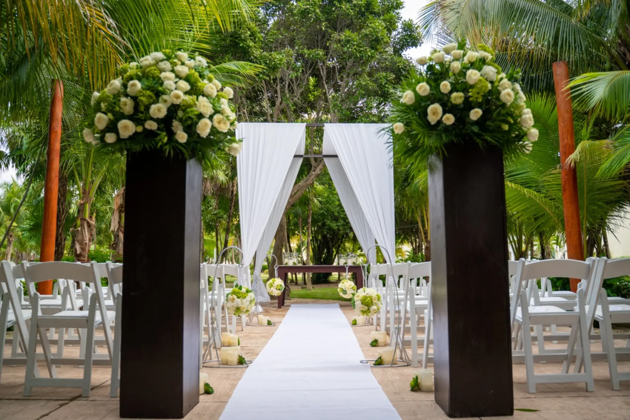 Garden wedding ceremony setup with white floral pillars and drapes at El Dorado Royale, Riviera Maya