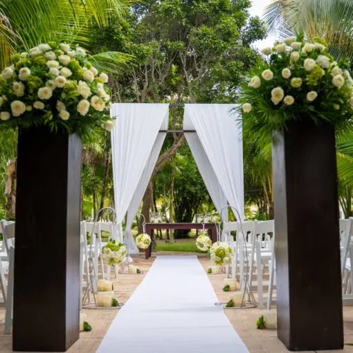Garden wedding ceremony setup with white floral pillars and drapes at El Dorado Royale, Riviera Maya