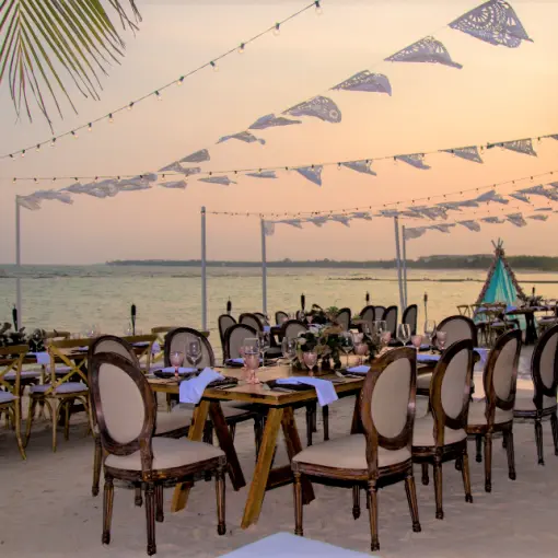 Beachfront wedding reception setup with wooden tables and string lights at El Dorado Seaside Palms, Riviera Maya