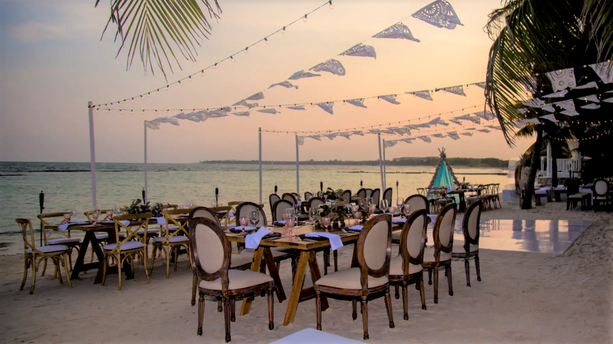 Beachfront wedding reception setup with wooden tables and string lights at El Dorado Seaside Palms, Riviera Maya
