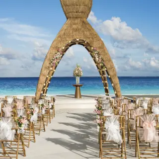 Beachfront wedding ceremony with a thatched arch and bamboo chairs at Dreams Aventuras, Riviera Maya