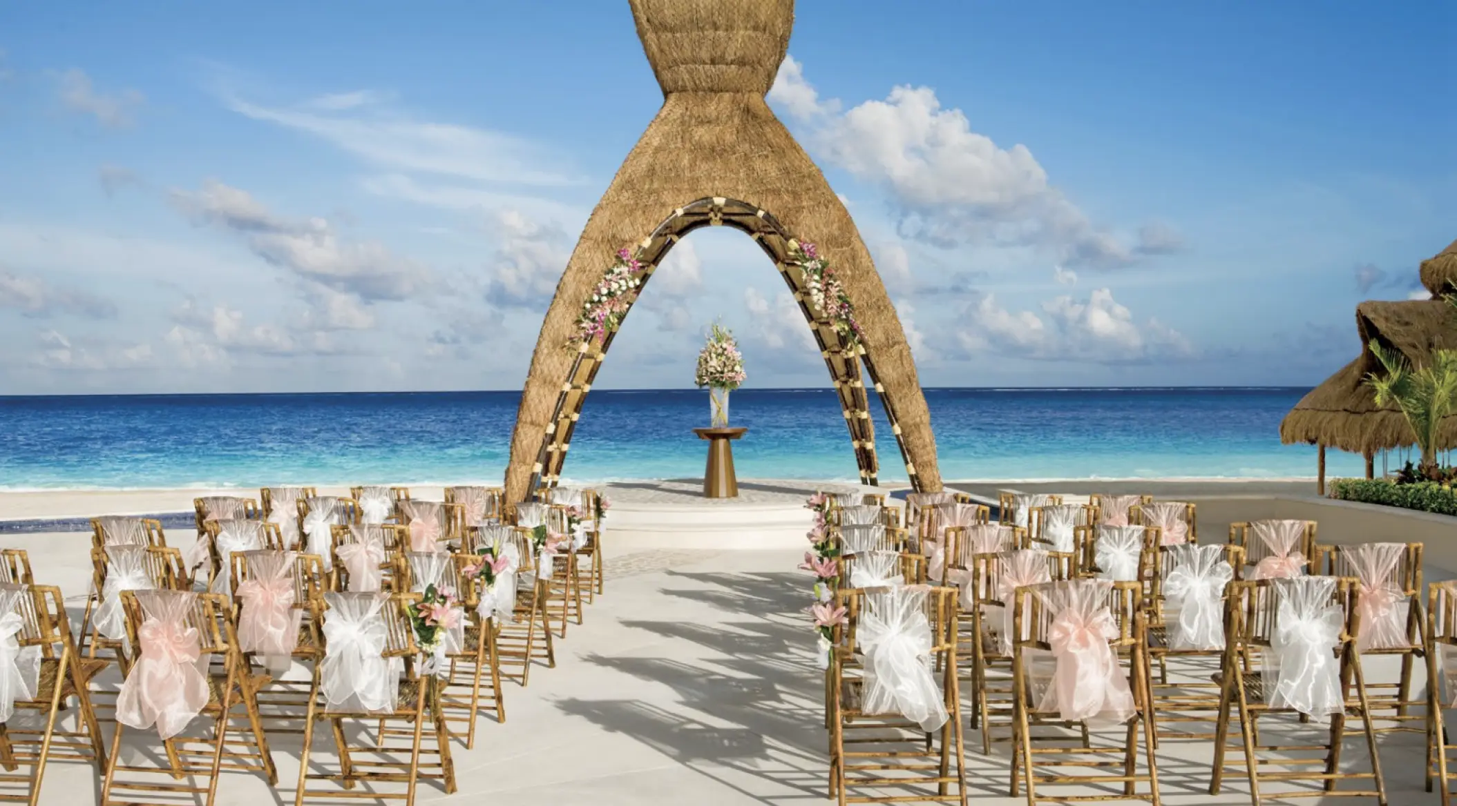Beachfront wedding ceremony with a thatched arch and bamboo chairs at Dreams Aventuras, Riviera Maya