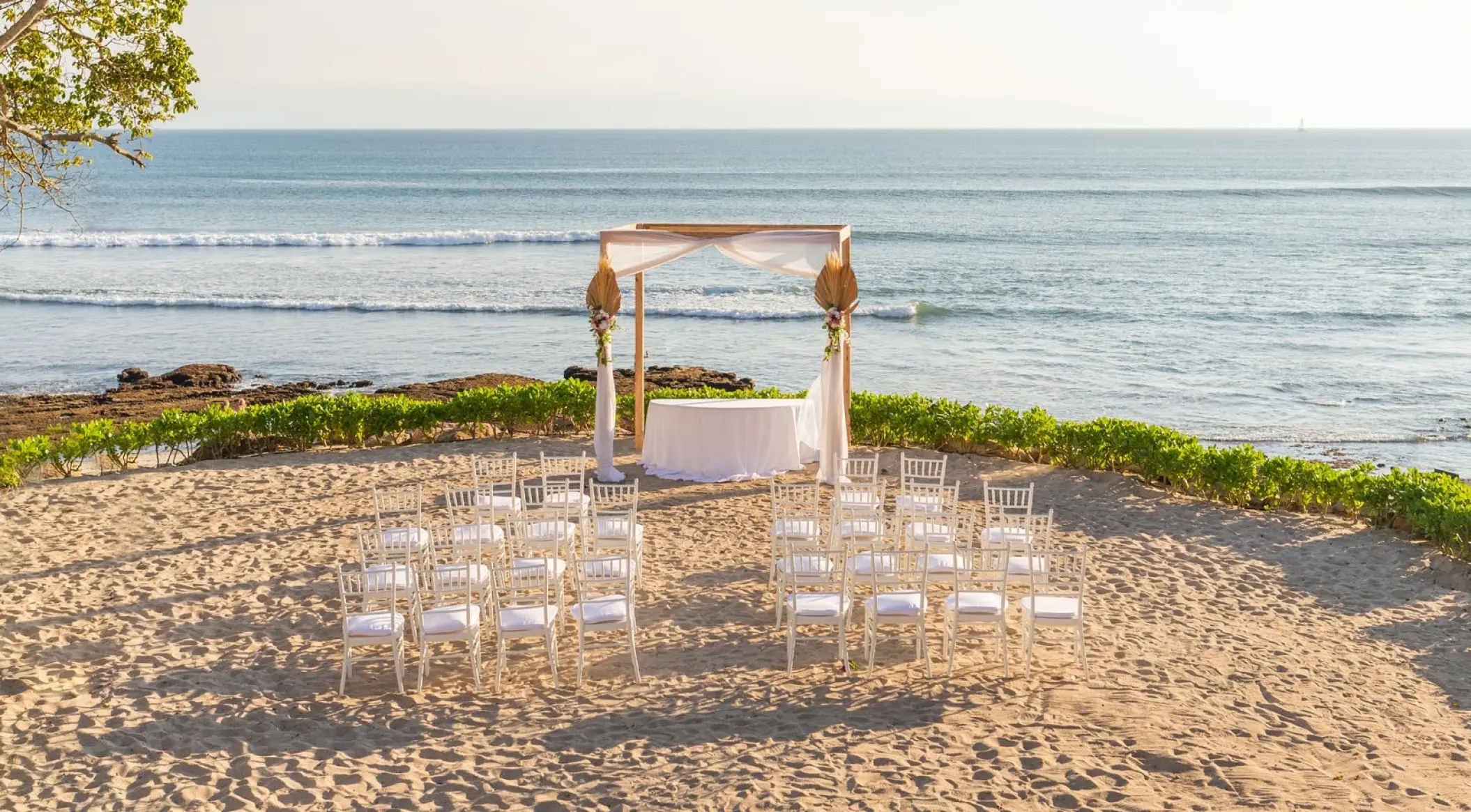 Beachfront wedding ceremony with a wooden arch and white chairs at Dreams Bahia Mita, Puerto Vallarta