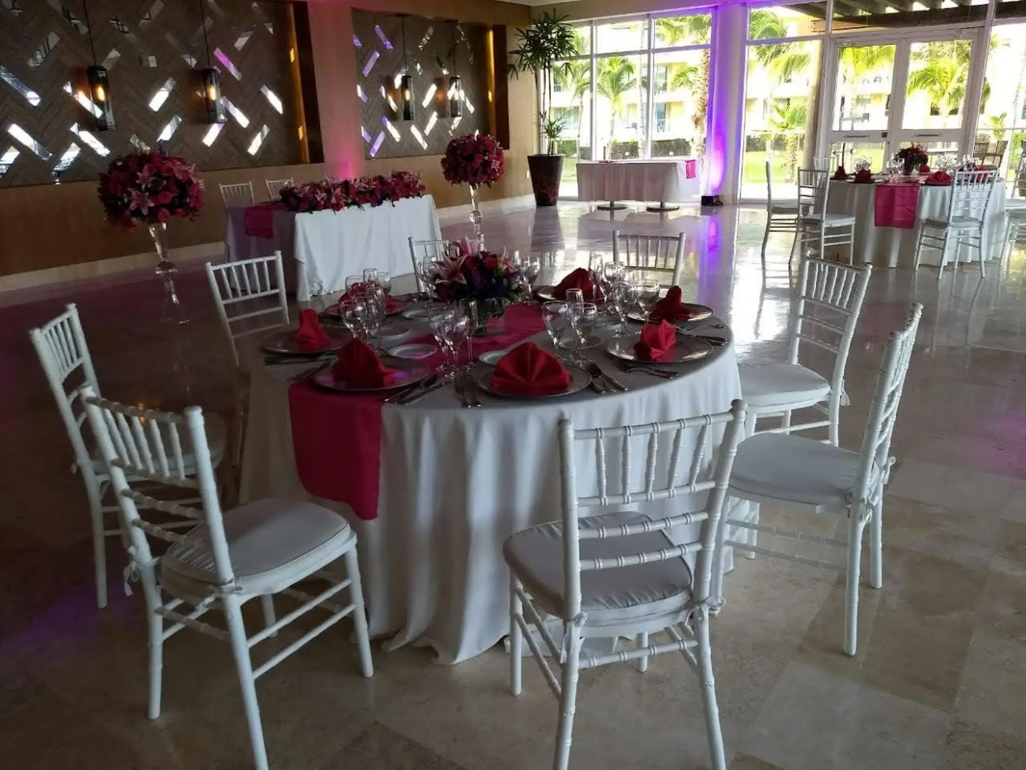 Indoor wedding reception with white chairs and pink floral centerpieces at Dreams Jade, Riviera Maya