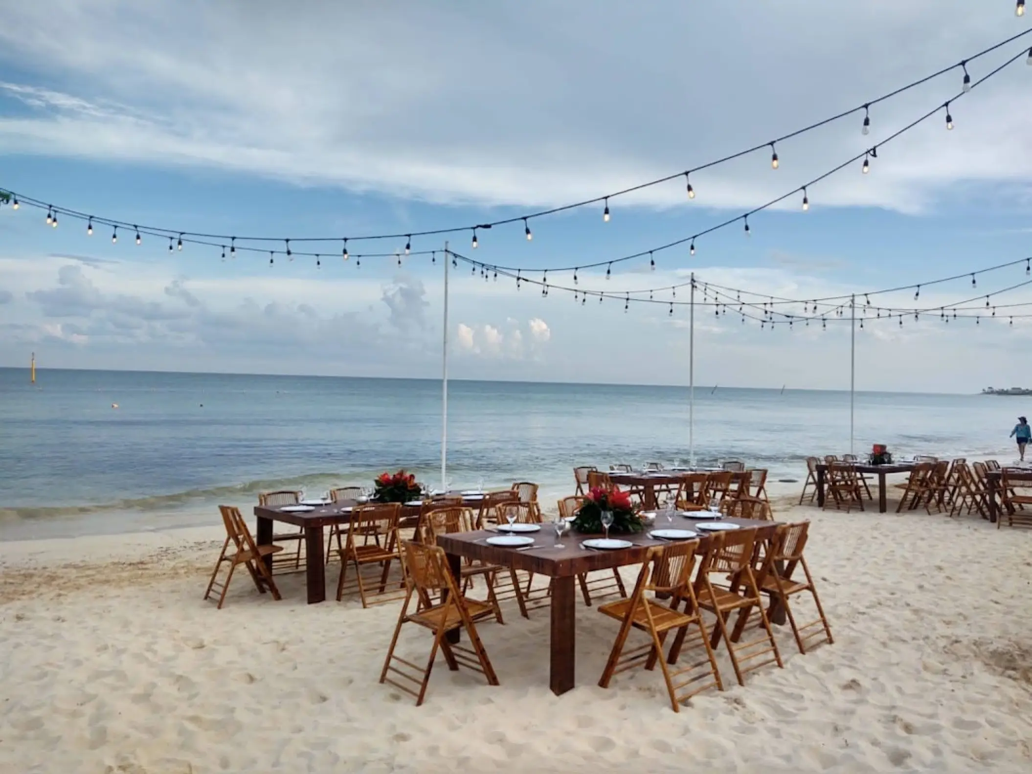 Beachfront wedding reception setup with wooden tables and string lights at Dreams Jade, Riviera Maya