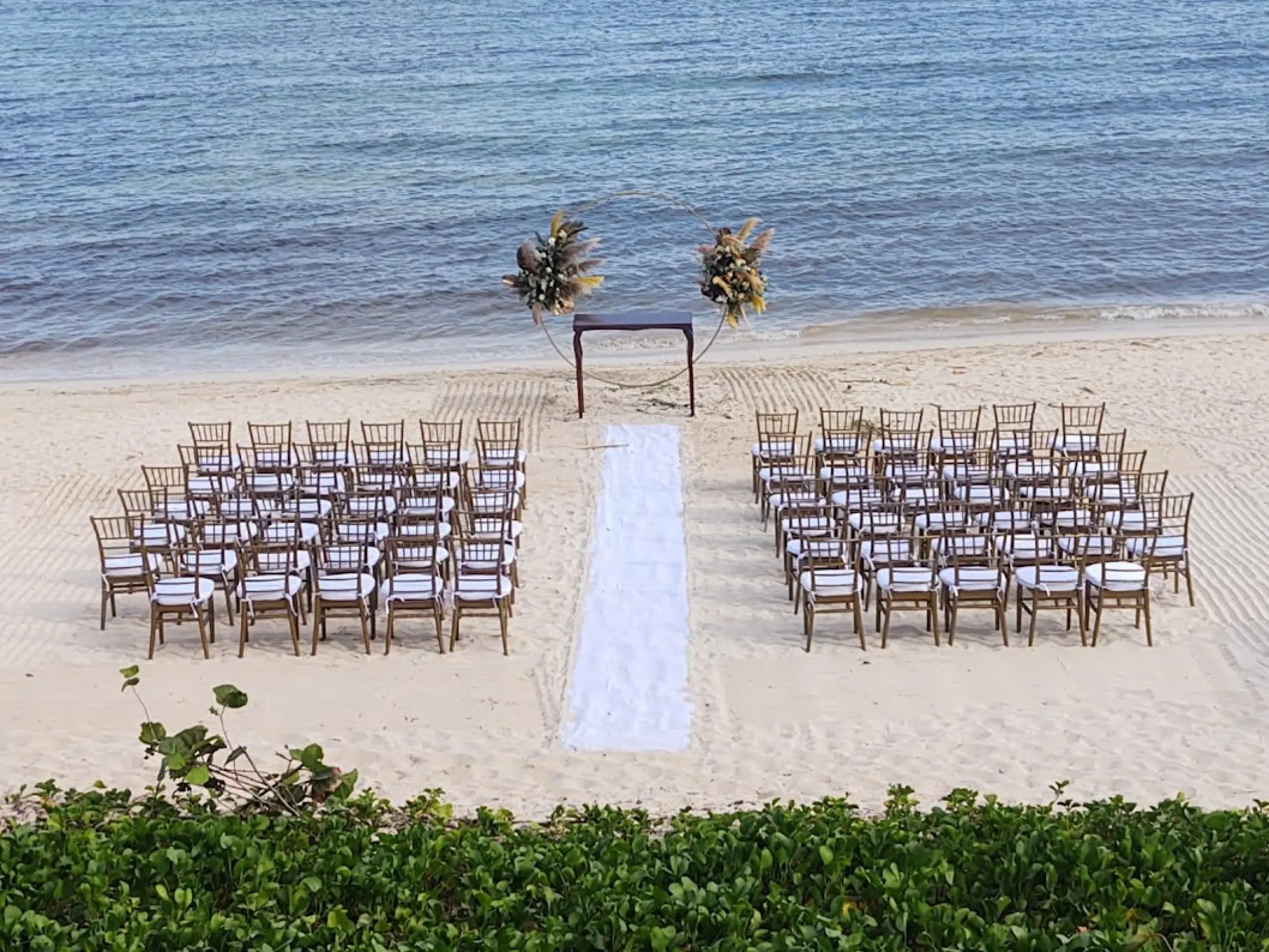 Beachfront wedding ceremony with wooden chairs and a white aisle runner at Dreams Jade, Riviera Maya