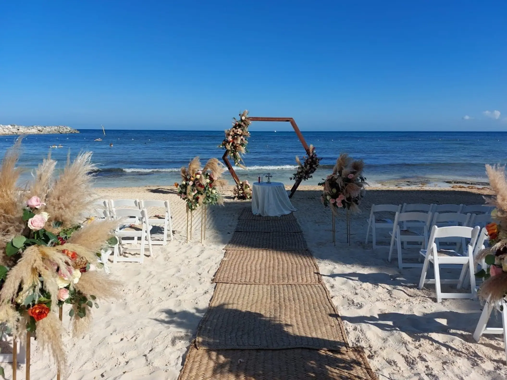 Beachfront wedding ceremony with a hexagonal arch and pampas grass at Dreams Jade, Riviera Maya