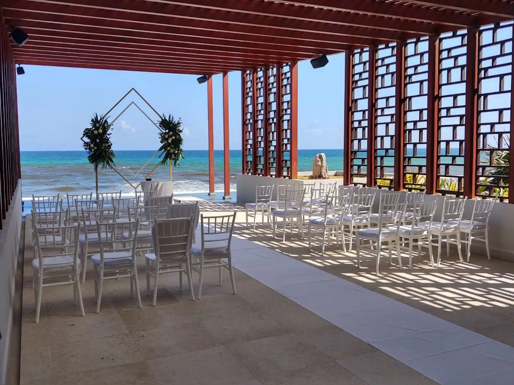 Pergola deck wedding ceremony with white chairs and ocean views at Dreams Jade, Riviera Maya
