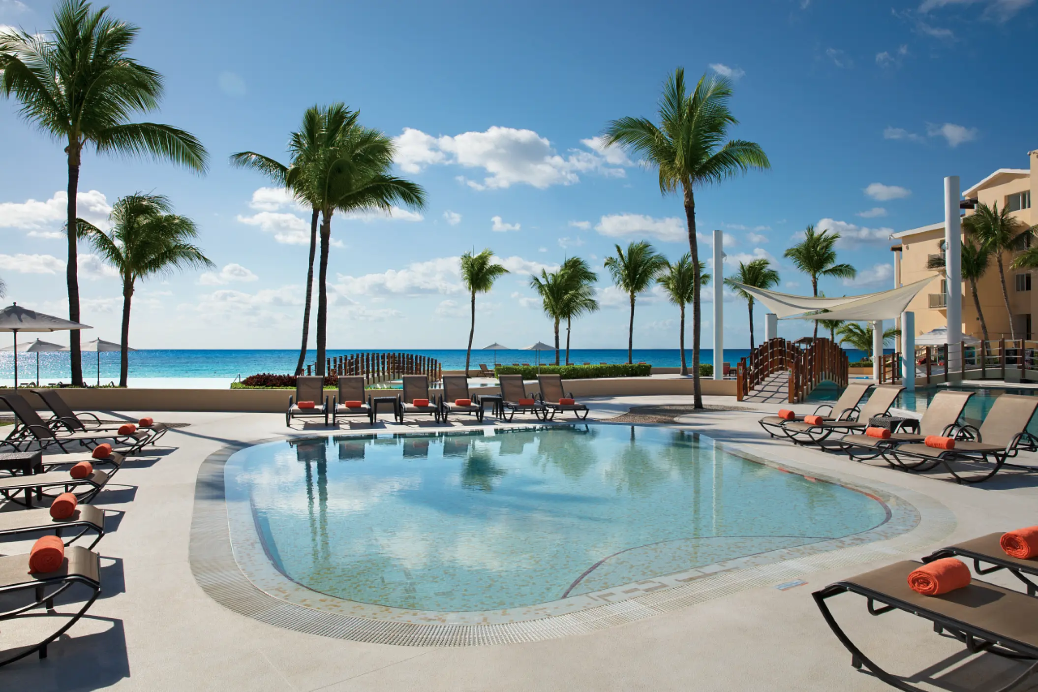 Dreams Jade swimming pool with lounge chairs and palm trees by the ocean, Riviera Maya