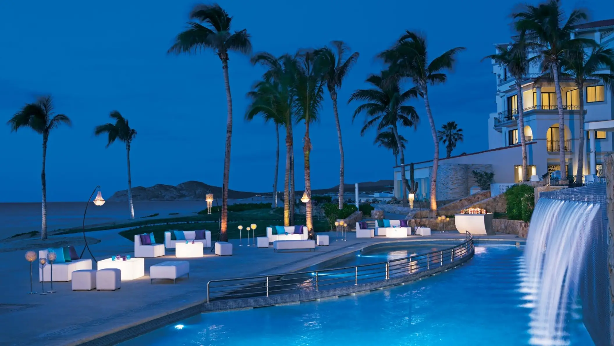 Cascada pool and terrace lit at night with a waterfall feature at Dreams Los Cabos, Cabo San Lucas