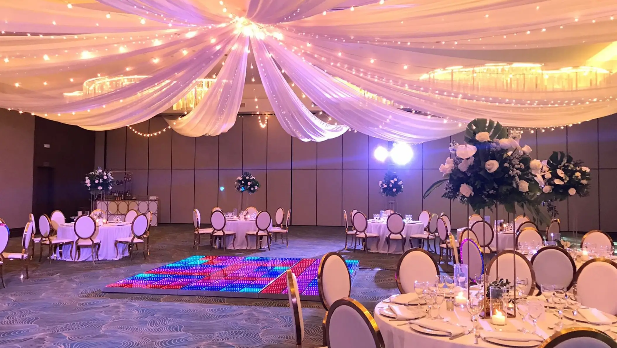 Indoor ballroom wedding reception with fabric ceiling draping and a lighted dance floor at Dreams Macao Beach, Punta Cana