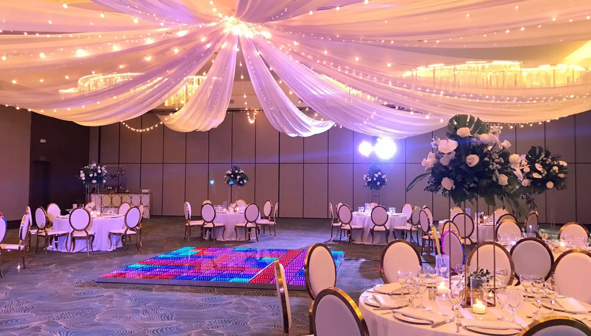 Indoor ballroom wedding reception with fabric ceiling draping and a lighted dance floor at Dreams Macao Beach, Punta Cana