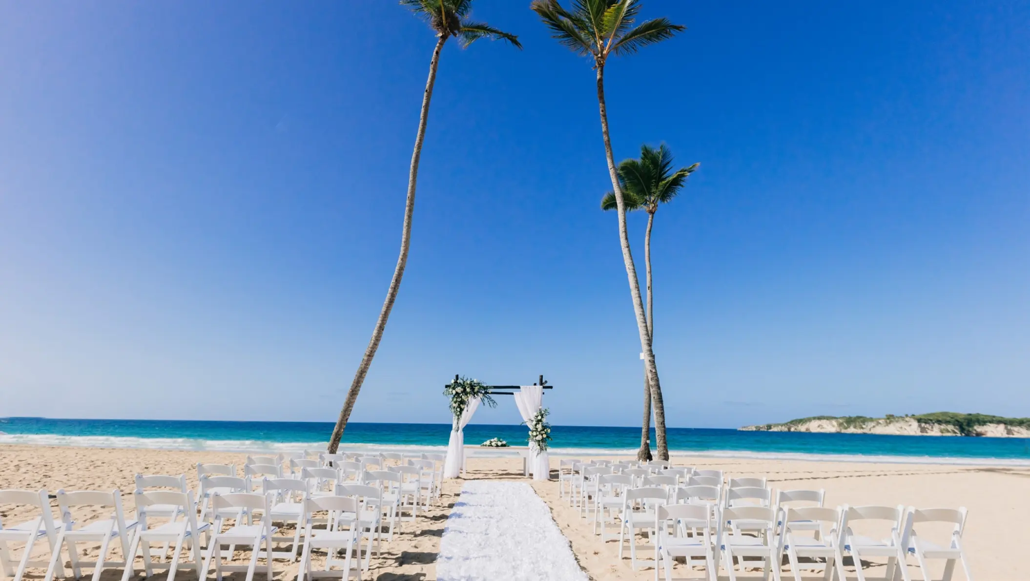 Beachfront wedding ceremony with white chairs and floral arch at Dreams Macao Beach, Punta Cana